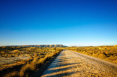 Dirt road along countryside landscape against clear blue sky