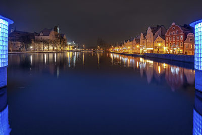 Illuminated buildings by river against sky at night