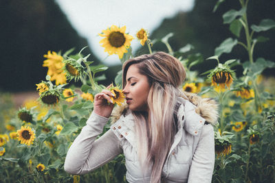 Young woman with eyes closed smelling sunflowers while sitting at park