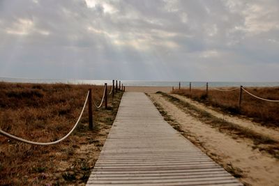 Boardwalk leading towards sea against sky