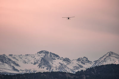 Airplane flying over snowcapped mountains against sky during sunset