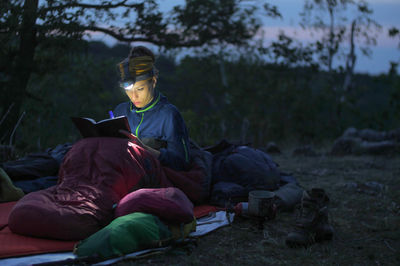 Woman writing on book while camping on field at dusk