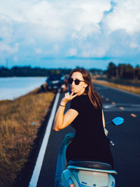 Portrait of young woman showing peace sign while sitting on motor scooter at road