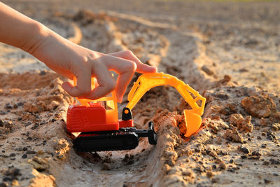 Person hand holding toy crane on sand