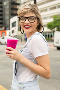 Portrait of smiling woman holding drink in city