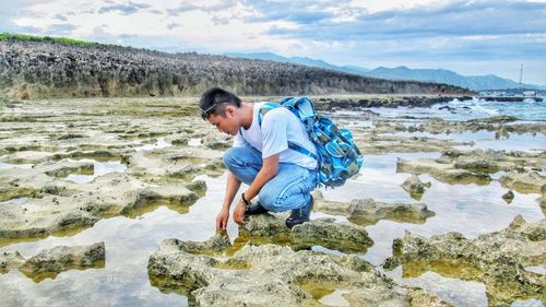 Man crouching on rocks amidst water