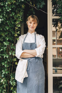 Portrait of smiling female chef standing with arms crossed outside restaurant