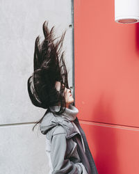 Close-up of woman with tousled hair against wall