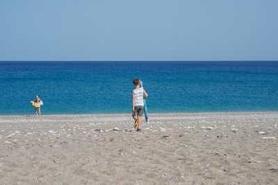 Woman standing on beach against clear blue sky
