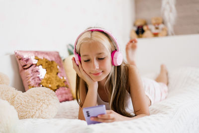 Teenager with headphones listens to music in bed, communicates on social networks in the morning