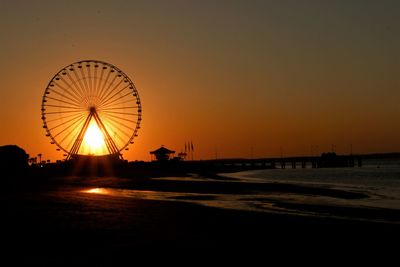 Silhouette ferris wheel at beach against clear sky during sunset