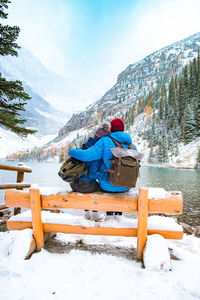 People sitting on bench by snowcapped mountains during winter