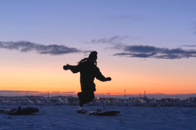 Silhouette man on sea against sky during sunset