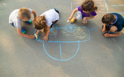 High angle view of girls and boys drawing with chalk on road