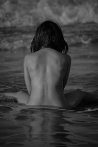 Rear view of sensuous naked woman sitting on shore