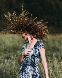 Young woman standing by tree on field