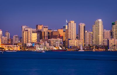 Illuminated buildings in city against clear blue sky