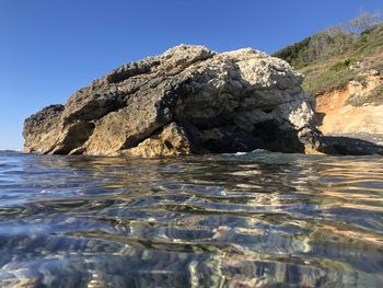 Rock formation in sea against clear blue sky