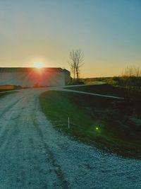 Road by field against sky during sunset