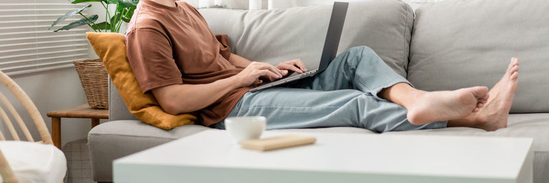 Cropped image of man using laptop while sitting on sofa