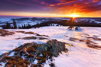 Snow covered landscape against sky during sunset