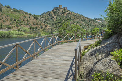 Footbridge over plants by mountains against sky