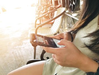 Midsection of woman using mobile phone while sitting on chair