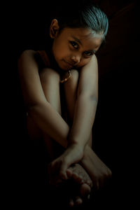 Girl sitting against black background