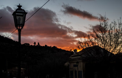 Low angle view of street light by building against sky at sunset