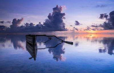 Wooden posts in lake against sky at sunset