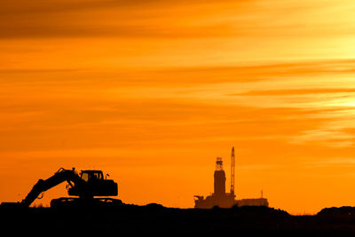 Silhouette factory against sky during sunset