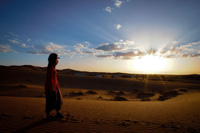Rear view of woman standing on sand at sunset
