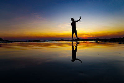 Silhouette man taking selfie while standing on shore against sky during sunset
