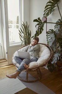 Woman sitting in papasan chair and using laptop