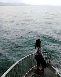 Rear view of woman sitting on railing against sea