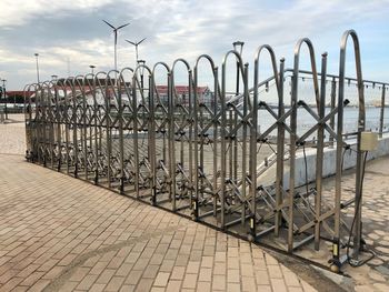 Metallic railing on footpath by street against sky