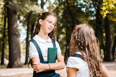 Two female students in school uniforms are talking in the park on a warm day