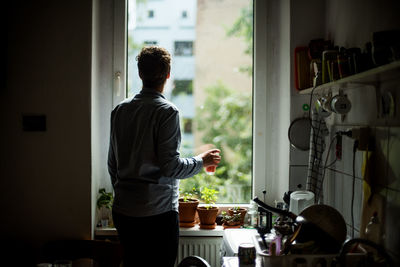 Rear view of person looking out kitchen window