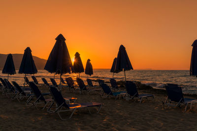 Chairs on beach against orange sky