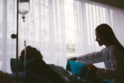 Female doctor putting blanket on male patient lying on bed in hospital