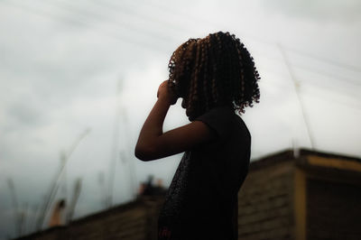 Girl with curly hair standing against sky