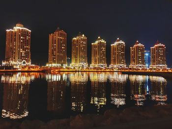 Illuminated buildings by river against sky at night