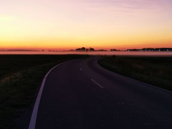 Empty road amidst field against sky during sunset