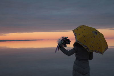 Woman photographing sea against sky during sunset