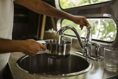 Midsection of man filling water through faucet in camper trailer