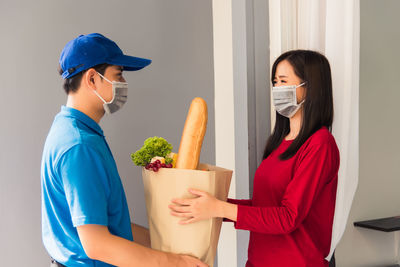 Delivery person wearing mask giving food to client outdoors