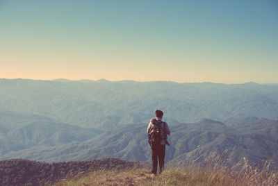 Rear view of young man standing on cliff against mountains