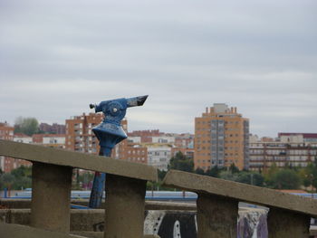 Bird on railing against sky in city
