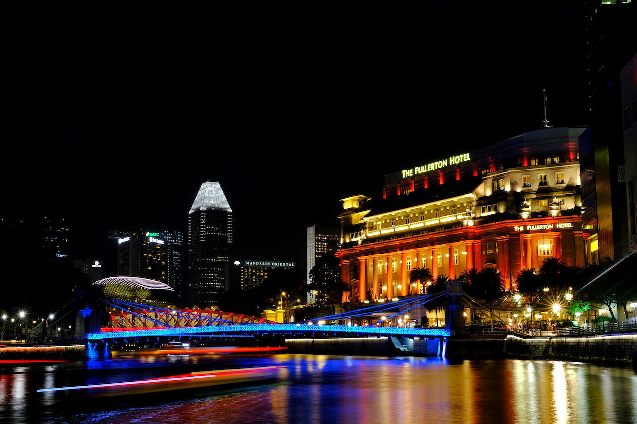 ILLUMINATED BRIDGE OVER RIVER AMIDST BUILDINGS AGAINST SKY AT NIGHT