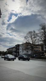 Cars parked on street by buildings in city against sky